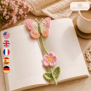 May include: A handmade crochet bookmark featuring a butterfly at the top with pink, cream, and orange wings, connected by a green stem to a pink flower with a yellow center and two green leaves, resting on the open pages of a hardcover book.