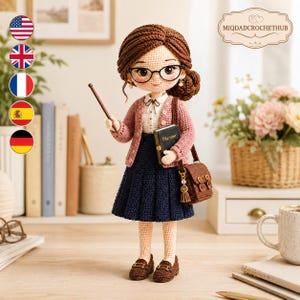 Pode incluir: Uma boneca de crochê com cabelo castanho em um coque, usando óculos de aro preto, um cardigã rosa sobre uma camisa branca de colarinho e uma saia plissada azul-marinho. A boneca segura um ponteiro marrom e uma agenda preta com a palavra Planner.