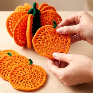 Puede incluir: Un juego de posavasos de ganchillo con forma de calabaza naranja, con un diseño circular y un pequeño tallo verde en la parte superior. Los posavasos están apilados formando una calabaza tridimensional, con piezas sueltas al lado.