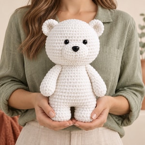 May include: A white crocheted teddy bear toy featuring a rounded head, small ears, and a textured yarn surface. The bear has two small black circular eyes and a black oval nose, with a simple, compact body shape and short arms and legs.