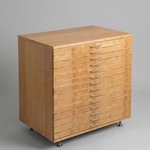 Könnte beinhalten: Ein flacher Aktenschrank aus hellem Holz mit zwölf übereinanderliegenden Schubladen. Jede Schublade ist mit einem schmalen, horizontalen, silberfarbenen Metallgriff versehen. Der Schrank steht auf vier kleinen, dunklen Metallfüßen.