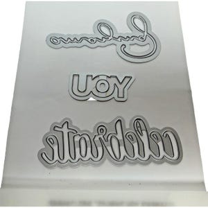 May include: A set of three silver-colored metal cutting dies for crafting. The dies feature the words "Celebrate" in a cursive script, "JOY" in a bold block font, and another cursive word that appears to be "Endearment" or similar.