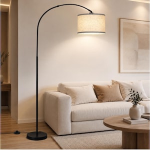 May include: A tall floor lamp with a slender black metal arched pole and a circular base. The lamp features a cylindrical drum shade made of textured beige fabric, which emits a warm, soft glow from the light source contained within the shade.