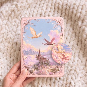May include: A rectangular e-reader case featuring a fantasy illustration of a castle nestled in mountains with two flying dragons against a pastel sky. A circular inset shows a zoomed-in view of the dragons amidst pink clouds and cherry blossoms.