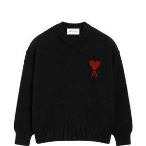 Könnte beinhalten: Ein schwarzer Langarmpullover mit Rundhalsausschnitt und gerippten Bündchen an Kragen, Ärmeln und Saum. Auf der Brust befindet sich ein rotes, gesticktes Herz-Logo mit einem integrierten Buchstaben A. Ein weißes Markenetikett ist im Kragen sichtbar.