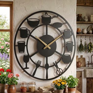 May include: A large circular black metal wall clock featuring a skeleton design with gold-coloured hands. The frame incorporates silhouettes of kitchen items including a saucepan, bowl, mugs, glasses, a fork, and scissors around the centre dial.