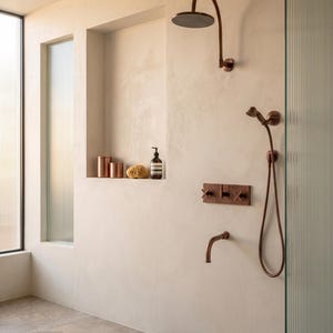 May include: A copper shower system featuring a wall-mounted rainfall showerhead, a handheld shower wand with a flexible hose, a bath spout, and a rectangular control plate with two cross-handle valves, set against a smooth beige wall.