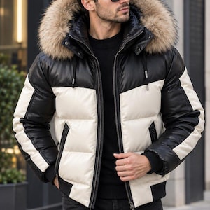 Puede incluir: Una chaqueta acolchada de bloques de color con una sección superior negra y una sección inferior blanca con mangas negras. La chaqueta incluye una capucha con un borde grueso de piel sintética marrón, cierre de cremallera y dos bolsillos.