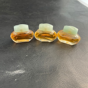 May include: Three small, clear glass perfume bottles with light green tops. The bottles are filled with a light amber liquid.