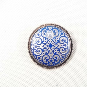 May include: A silver brooch with a blue and silver enamel design. The design features a repeating pattern of swirls and dots.