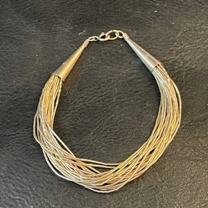 May include: A silver chain bracelet with multiple strands of small, round beads. The bracelet has a clasp fastening.