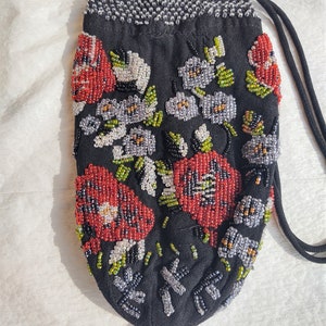May include: Black beaded pouch with a drawstring closure, adorned with red, white, and gray beaded floral designs. The pouch features a beaded bottom and a beaded top edge. A black drawstring is attached.