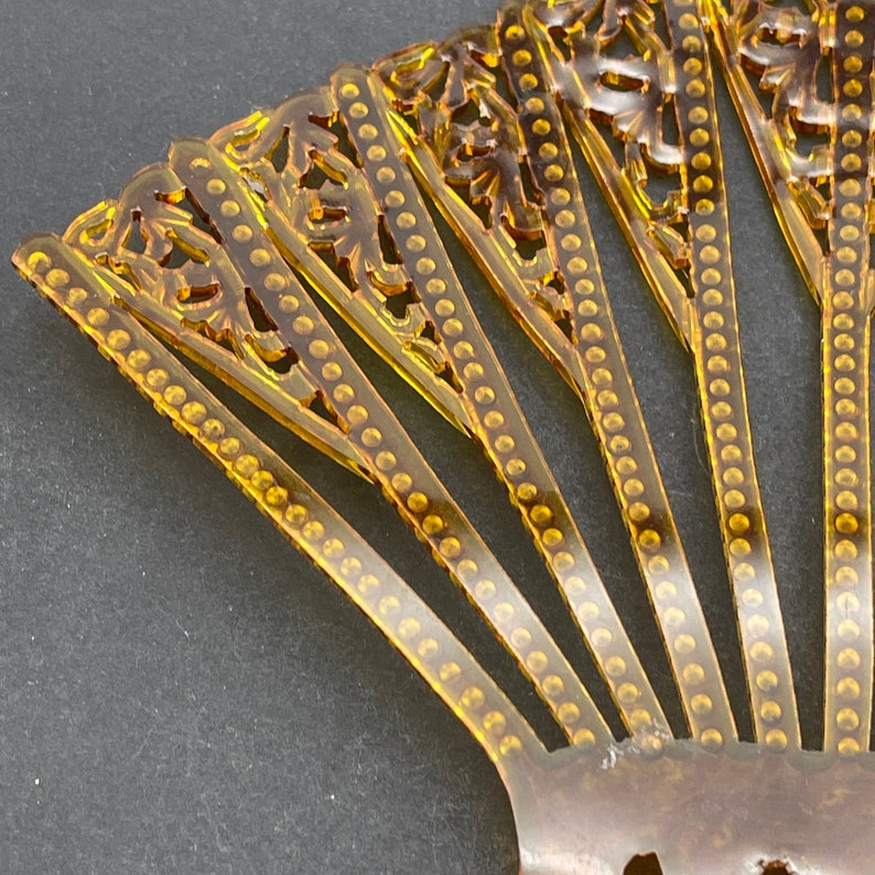 May include: A vintage amber plastic hand fan with a decorative design of circles and floral patterns.