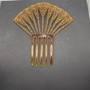 May include: A brown plastic hair comb with a decorative fan-shaped design. The design features intricate details and is accented with colorful rhinestones.