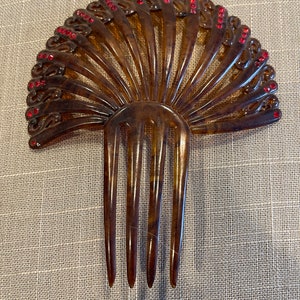 May include: A brown tortoiseshell hair comb with a fan-shaped design and red rhinestone accents.