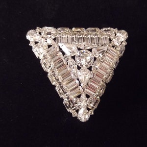 May include: A triangular brooch with a silver tone finish, featuring a cluster of clear rhinestones in a geometric pattern.