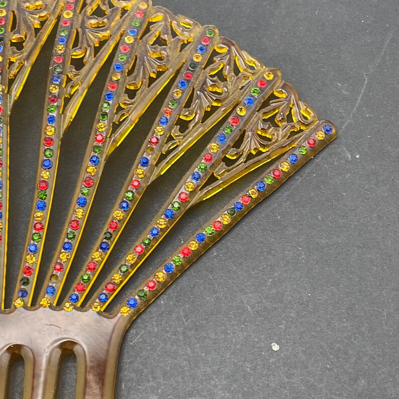 May include: A vintage hair comb with a fan-shaped design. The comb is made of brown plastic and features a decorative pattern with colorful rhinestones.