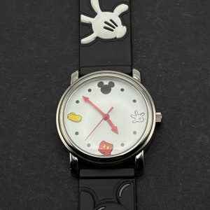 May include: A black and white Mickey Mouse watch with a silver face and black silicone band. The watch face features Mickey Mouse's head, hands, and shoes as hour markers.