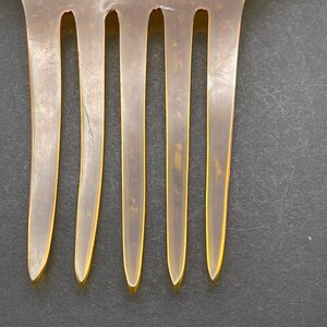 May include: A close-up of a brown comb with five teeth. The comb is made of a translucent material and has a slightly curved shape.