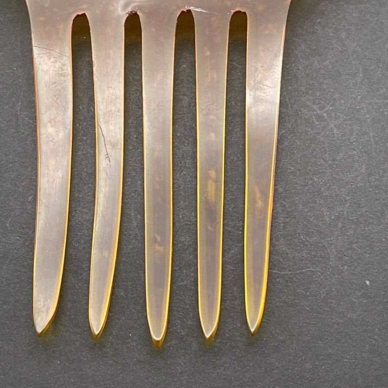 May include: A close-up of a brown comb with five teeth. The comb is made of a translucent material and has a slightly curved shape.