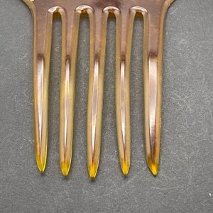 May include: A close-up of a brown plastic comb with five teeth. The comb is made of a translucent material and has a slightly rounded shape.