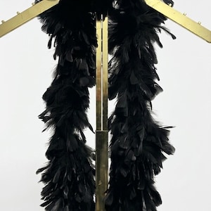 May include: A long, voluminous black feather boa draped over a gold-toned metal garment rack. The boa consists of dense, soft black feathers that hang vertically, creating a textured, layered appearance across the metallic frame structure.