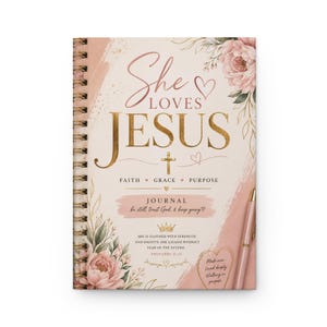 May include: A spiral-bound journal with a cream cover featuring pink floral illustrations, gold text reading She Loves Jesus, Faith, Grace, Purpose, and Proverbs 31:23. A light pink pen rests on the right side of the cover against a brushstroke design.