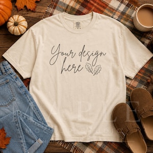 May include: A cream-colored short-sleeve t-shirt featuring the dark brown text "Your design here" accompanied by a small line-art illustration of two oak leaves. The shirt has a crew neckline and a standard fit, displayed on a flat surface.