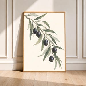 Può includere: Una stampa artistica da parete verticale incorniciata che presenta un'illustrazione botanica di un ramo di ulivo con cinque olive viola scuro e foglie allungate verde salvia su uno sfondo color crema in una sottile cornice in legno chiaro.