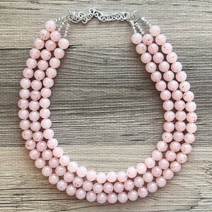 May include: A multi-strand necklace made of pink beads with a speckled pattern. The necklace is made of three strands of beads and has a silver clasp.