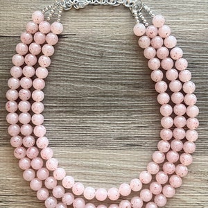 May include: A three-strand pink beaded necklace with a silver chain clasp. The beads are round and have a speckled texture.