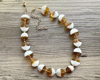 May include: A white and brown glass bead necklace with a gold chain. The beads are round and have a swirling pattern.