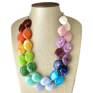 Puede incluir: Un collar multicolor con cuentas grandes, redondas y planas en un patrón de arcoíris. Las cuentas están hechas de un material translúcido con remolinos de color.