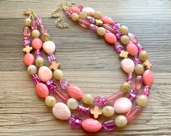 May include: A multi-strand necklace with pink and beige beads, featuring gold accents and small pink flower charms.
