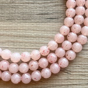 May include: A strand of pink and white speckled beads. The beads are round and have a frosted finish.