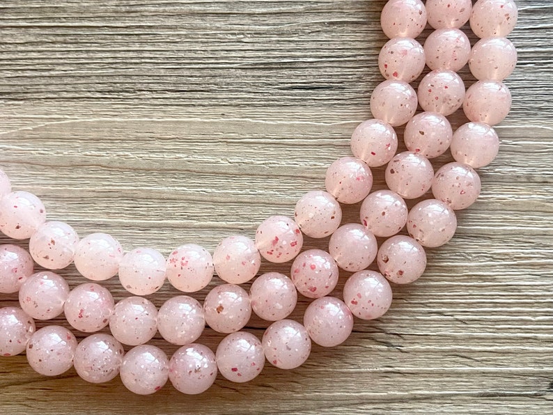 May include: A strand of pink and white speckled beads. The beads are round and have a frosted finish.