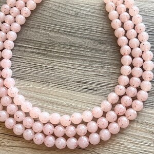 May include: A strand of pink and white speckled beads, arranged in a circle on a wooden surface.
