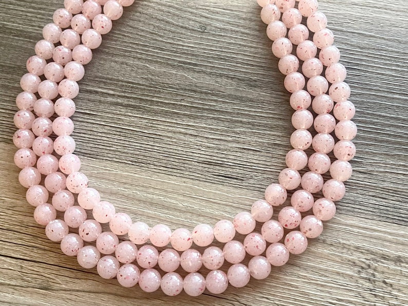 May include: A strand of pink and white speckled beads, arranged in a circle on a wooden surface.