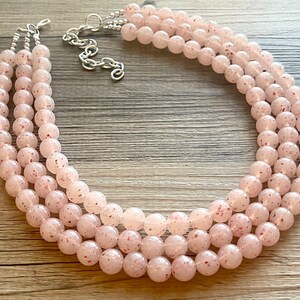 May include: A three-strand necklace made of pink and white speckled beads. The necklace is made of round beads and has a silver clasp.
