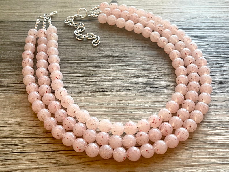 May include: A three-strand necklace made of pink and white speckled beads. The necklace is made of round beads and has a silver clasp.