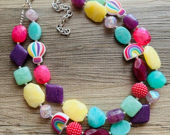 May include: A colorful multi-strand necklace with various shaped beads, including yellow, pink, purple, green, and red. The beads feature a hot air balloon and rainbow design.