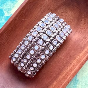 May include: A silver bracelet with multiple rows of small, clear, iridescent stones. The bracelet is on a wooden surface.