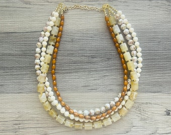 May include: A multi-strand necklace with brown, white, and beige beads. The necklace is made of different shapes and sizes of beads, including round, square, and rectangular beads.