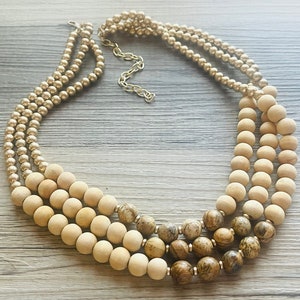 Op de afbeelding: Een meerrijige ketting met houten kralen in natuurlijke en bruine tinten. De ketting heeft een gouden ketting en een gelaagd ontwerp.