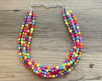 Puede incluir: Collar multicadena hecho de cuentas redondas de colores. El collar está hecho de cinco cadenas de cuentas en varios colores, incluyendo rojo, naranja, amarillo, verde, azul y morado. Las cuentas son todas del mismo tamaño y forma, y están enhebradas en una cadena plateada.