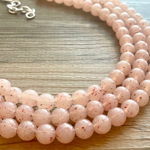 May include: A multi-strand necklace made of light pink beads with a speckled, translucent finish.