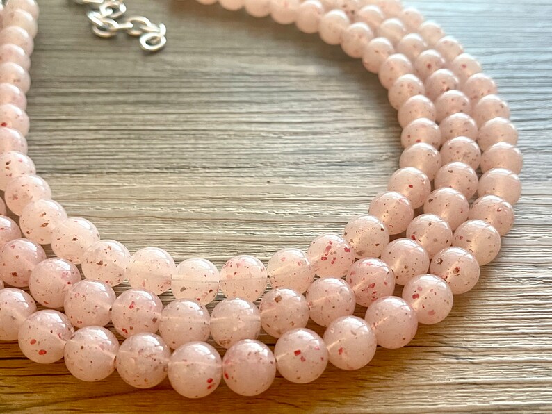 May include: A multi-strand necklace made of light pink beads with a speckled, translucent finish.