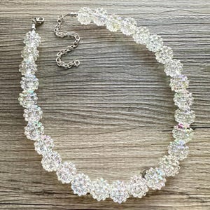May include: A clear crystal beaded necklace with a silver chain closure. The beads are faceted and iridescent, creating a shimmering effect.