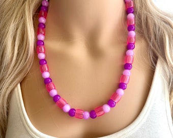 Puede incluir: Un collar de cuentas rosa, morado y rosa claro. Las cuentas son redondas y tienen un acabado brillante.