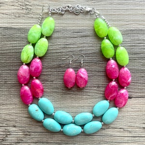May include: A three-strand necklace with large oval beads in shades of green, pink, and blue. Matching earrings with pink oval beads are included.